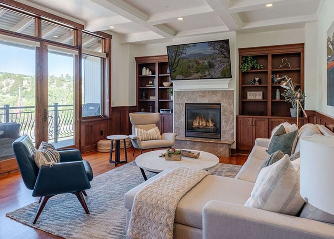 A luxurious living room in Victoria Condominiums 2 Bedroom features a fireplace, a television, comfortable seating, and a balcony with an exterior view.