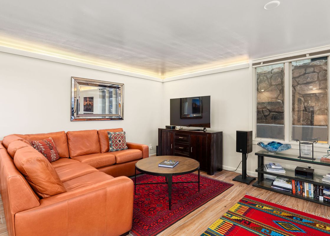 Cozy living area in Chateau Dumont Unit 23 with an orange leather sofa, a red oriental rug, a TV, and a large window.