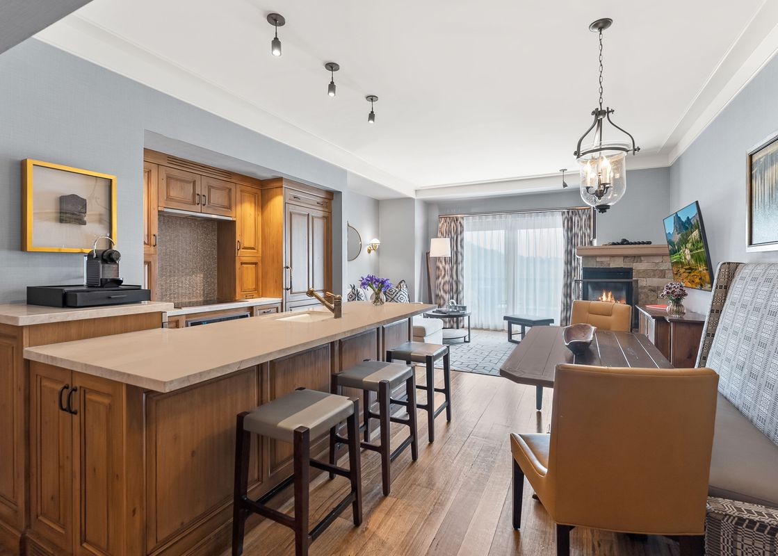 A modern open-concept living space features a kitchen island with bar stools, a dining area, and a living room with a fireplace and television, creating a sophisticated and comfortable ambiance.