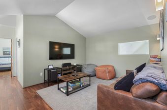 A cozy entertainment area with a large flat-screen TV, a media console, a leather sofa with pillows, bean bag chairs, and a coffee table with board games.
