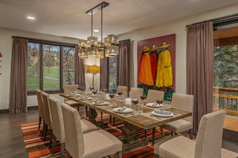 The dining area at Aspen Glade Retreat features a long wooden table set for a meal, surrounded by upholstered chairs.