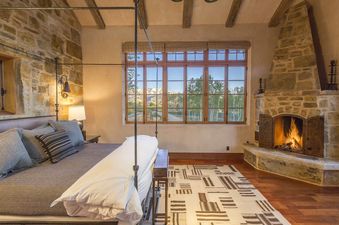 A bedroom with a king-sized bed, stone walls, and a fireplace.