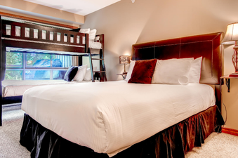 A spacious bedroom features a comfortable queen-size bed with crisp white linens and a dark brown headboard, along with a wooden bunk bed and a twin bed, offering ample sleeping arrangements.