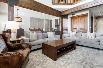 A spacious and inviting living room and kitchen area at Silver Star 33 with gray sofas, a wooden coffee table, and rustic wooden beams.