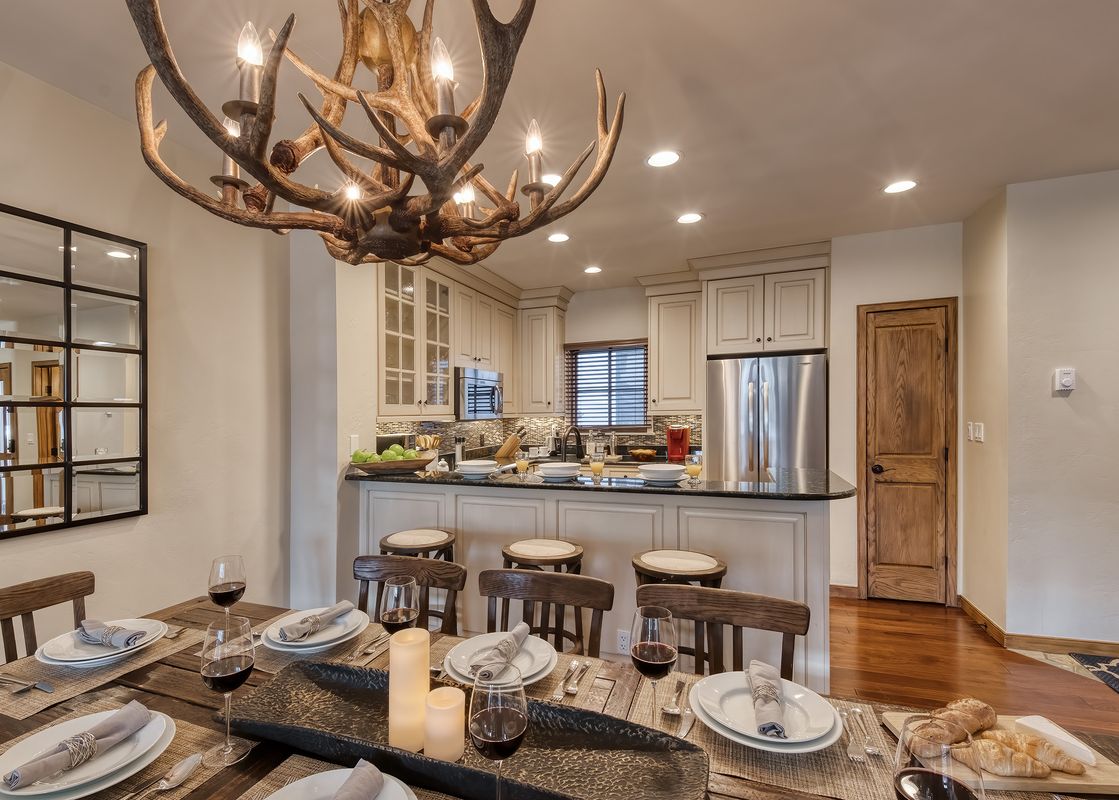 The dining area and kitchen of Chalet Fortessa, featuring a rustic antler chandelier and a fully set wooden dining table.