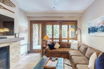 A cozy living room with a leather sectional sofa, a fireplace, and large windows offering a view of the outdoors.