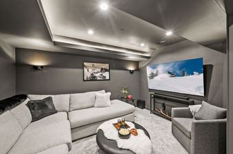 A modern home cinema room with a large TV, plush seating, and warm lighting at Bluebird Chalet Park City.