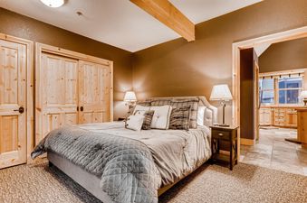 The bedroom is a tranquil retreat, featuring a large, inviting bed adorned with plush bedding, set against warm, earthy tones on the walls.