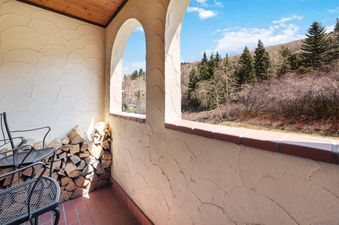 A private patio featuring rustic red tiled floors, textured cream stucco walls, and arched openings that frame views of a forested mountain landscape.