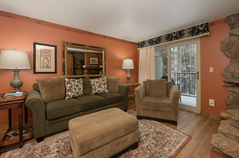 The living room at Beaver Village 1514 is furnished with a comfortable green sofa, a matching ottoman, and a plush armchair, all centered around a rustic coffee table.