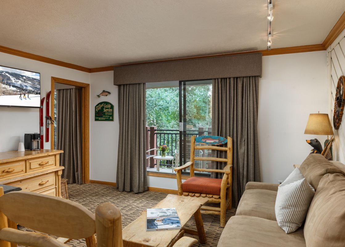 A cozy living area featuring a large window, a sofa, a coffee table, and a TV, with wooden furniture and fishing-themed decor.