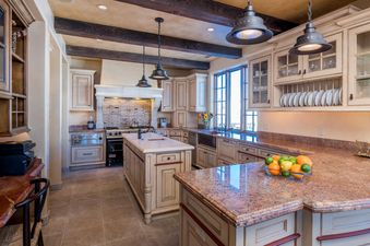 A spacious kitchen with large windows, exposed wooden beams, and a large island with granite countertops.