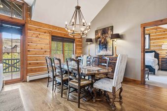 An elegant dining room at Buckhorn Townhome 264 with a large wooden table, chandelier, and a window offering mountain views.
