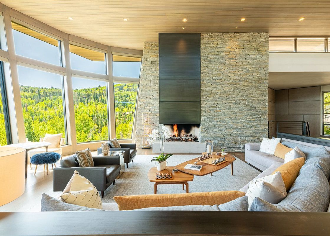 A luxury modern living room in Park City Colony Obsidian Ridge featuring a floor-to-ceiling stone fireplace and expansive windows with forest views.