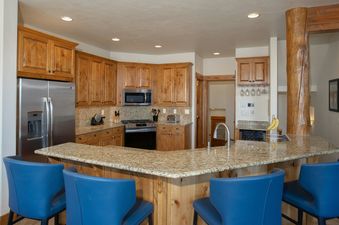 A spacious kitchen with wooden cabinets, granite countertops, and stainless steel appliances, including a large island with blue bar stools.