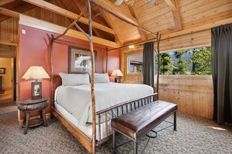 A rustic master bedroom in Rested Ridge Ski Haus with a four-poster bed, wood paneling, and a window view of trees and mountains.