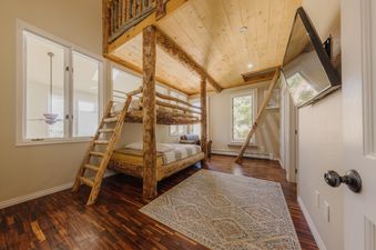 Rustic bedroom at Crystal Ridge featuring a custom log bunk bed with matching wooden ladders and beautiful hardwood floors.