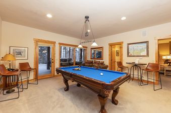 The game room at Fairview Lodge features a full-size billiards table with blue felt, multiple comfortable seating areas, and large windows that offer views of the snowy outdoors, creating a perfect space for entertainment.