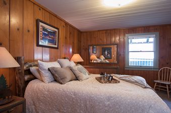 A cozy bedroom at North Shore Dancing Antler with rustic wood paneling, a large bed, and a window.
