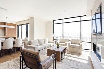 A bright and spacious open-concept living and dining area in Lift 406, featuring modern furnishings, large windows with city views, and warm wooden accents.