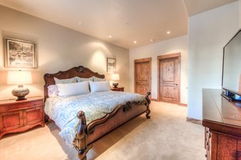 A master bedroom in Cowboy Heaven Luxury Suite Unit 2B with a large wooden bed, two nightstands with lamps, and rustic wooden doors.