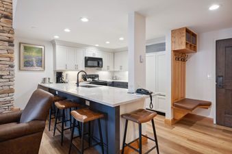 A modern kitchen with white cabinets, a large island with seating, and a stylish entryway with a wooden bench and coat hooks.