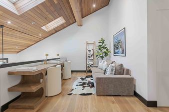 A modern and cozy loft office and sitting area at Queen Esther 2366 featuring a wood-paneled vaulted ceiling, a long desk with two white chairs, and a comfortable plush sofa.