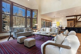 A living room with a large sectional sofa, two ottomans, and a coffee table, featuring a view of snow covered trees outside the window.
