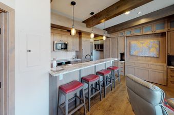 Kitchen with bar seating, a large living room, and an art piece above a fireplace.