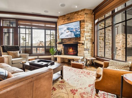 A cozy living room at Arrowleaf Lodge 302 with a stone fireplace, comfortable seating, and large windows offering views of the snowy mountain landscape.