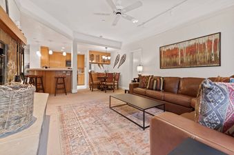 A spacious living room with a brown leather sofa, a fireplace, and an open-concept kitchenette and dining area featuring light wood cabinetry and rustic decor in The Charter B3305.