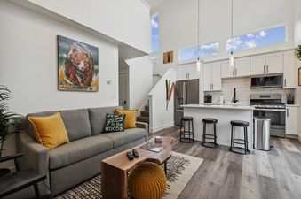 An open concept living room and kitchen area with a grey sofa, wooden coffee table, white kitchen cabinets, and stainless steel appliances at Quarry A21.