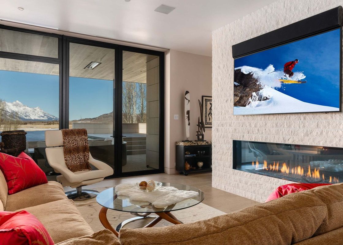 Modern living room at The Dragonfly Lodge with a sleek linear fireplace, wall-mounted television, and glass patio doors framing mountain views.
