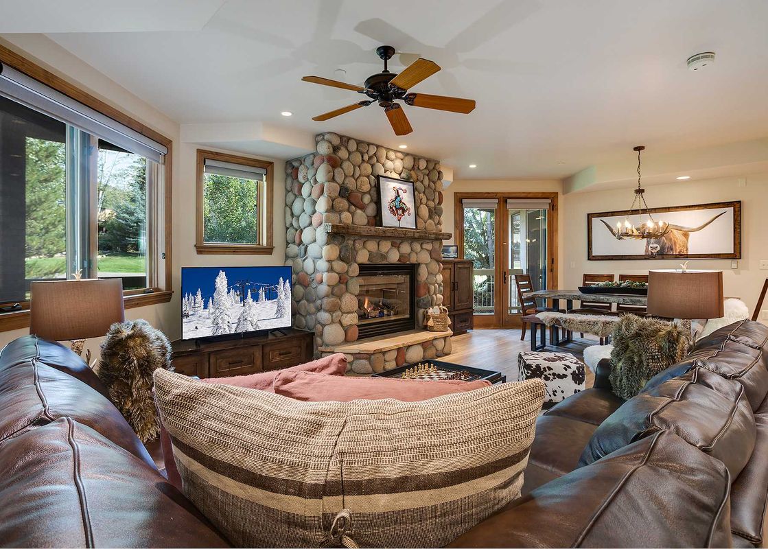 A spacious and inviting living area features a large leather sofa, a prominent stone fireplace, and a dining area, with natural light filtering through windows.