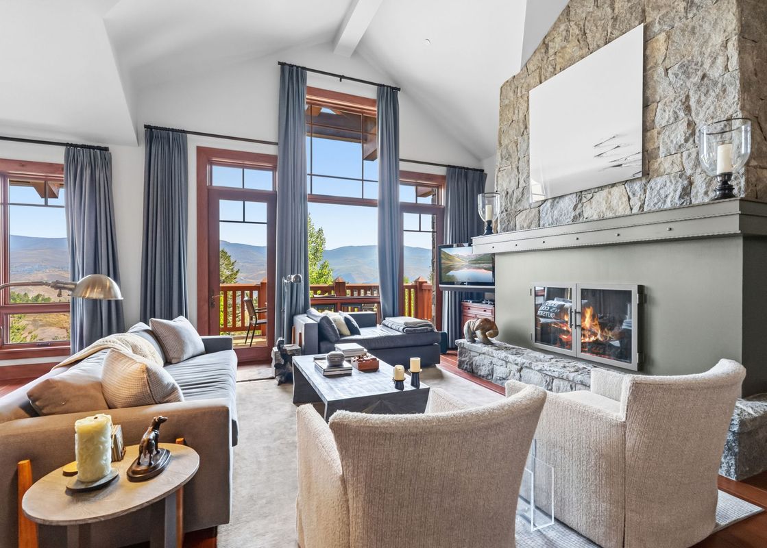 Spacious living room of the Hummingbird Overlook at Hummingbird Lodge with a stone fireplace and scenic mountain views through large windows.