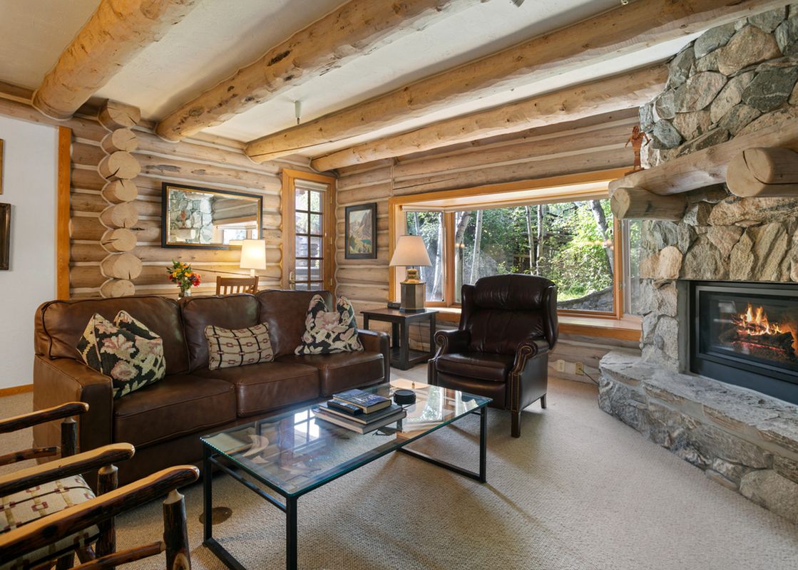 The living room of Pine Inn 09 features a fireplace with a stone hearth, leather furniture, and a large window overlooking the trees.