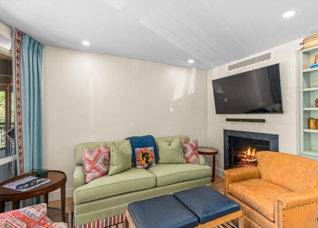 A living room with a green couch, two blue ottomans, a fireplace with a fire, and a bookshelf in the corner.