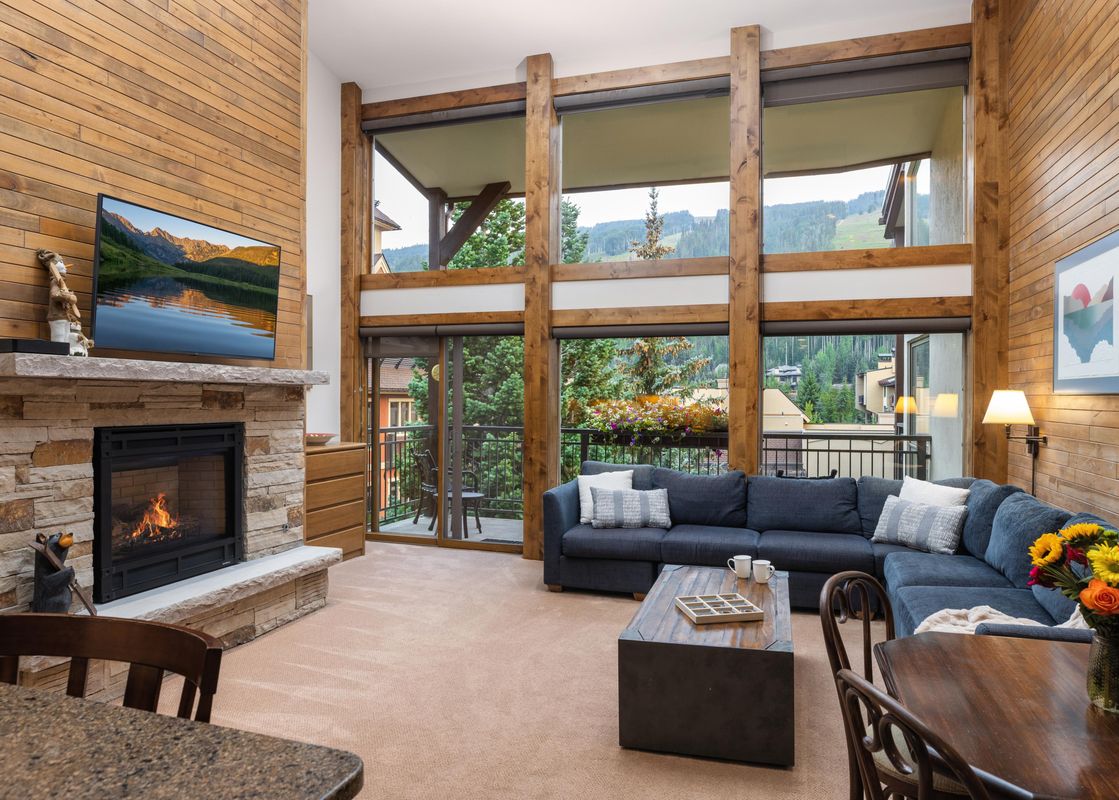A cozy living room at Montaneros 414 with a fireplace, a large sectional sofa, and expansive windows offering mountain views.