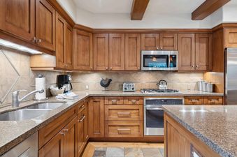 A modern kitchen with stainless steel appliances, wood cabinets, granite countertops, and a double sink.