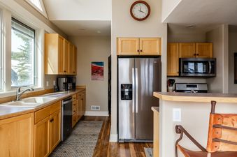 A modern kitchen with light wood cabinetry, stainless steel appliances, and a window offering a view of snowy trees.