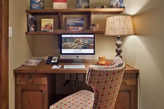 A cozy, well-lit office nook with a wooden desk, computer, and patterned chair, flanked by bookshelves and a table lamp.