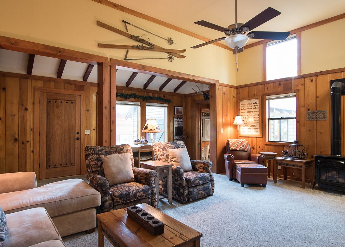 A cozy living room at the North Shore Dancing Antler features two armchairs, a chaise lounge, a rustic coffee table, a fireplace, and decorative skis on the wall.