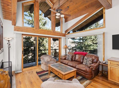 Bright living area in Crestwood 1212 with vaulted wood ceilings, a leather sofa, and large windows looking out on trees.