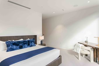 A modern bedroom in Founders Place 2503 with a king-sized bed featuring blue accents and a wooden writing desk with a white chair.