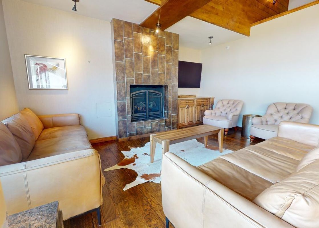 A living room with a fireplace, couches, and coffee tables, a brown leather couch is seen in the foreground.