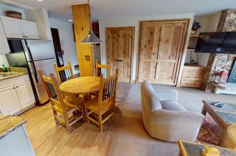The kitchen and dining area at Manor Vail 272 feature a rustic wood table with four chairs, a stainless steel refrigerator, and a granite countertop.