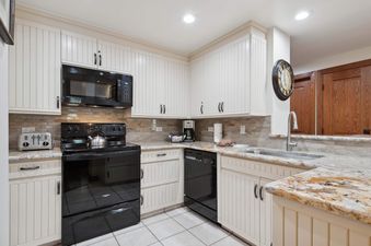 The pristine kitchen at The Charter E1505 features white cabinetry, granite countertops, and modern black appliances including a microwave, range, and dishwasher.
