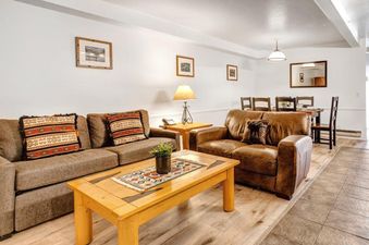 The comfortable living room at Suncreek A7 features a brown sofa with patterned pillows, a leather armchair, and a wooden coffee table, while the adjacent dining area showcases a wooden table and chairs.