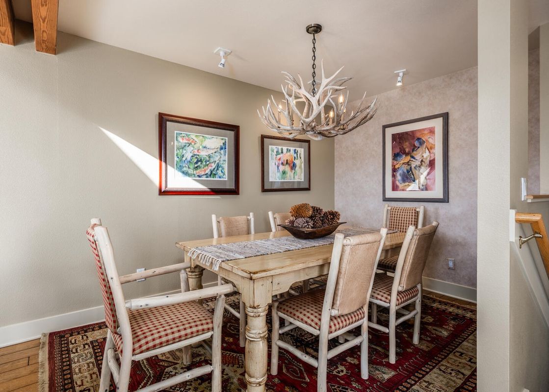 The dining area at Moonlight Basin Saddle Ridge F5 has a rustic wooden table with chairs, a chandelier made of antlers, and a red and white rug.