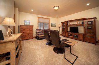 The media room features two leather recliners facing a large entertainment center with a TV, surrounded by wooden furniture and soft carpet.